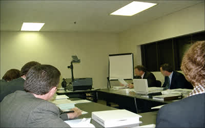 A low-resolution dated meeting-room photograph with anonymous staff and papers.