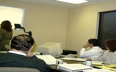 A low-resolution office meeting with anonymous staff and binders.