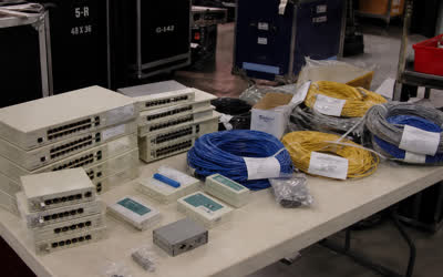 A low-resolution prep table with beige hubs, cable testers and coils of network cable in a warehouse.
