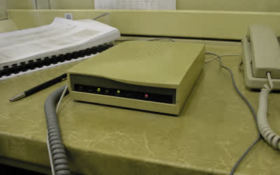 A low-resolution beige dial-up modem on a scratched desk beside a handset and paperwork.