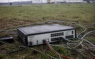 A low-resolution network switch in a muddy field with temporary cabling running in several directions.
