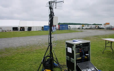 A low-resolution temporary wireless mast and equipment rack on an outdoor event field.