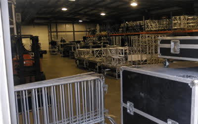A low-resolution equipment warehouse with truss, barriers and flight cases.
