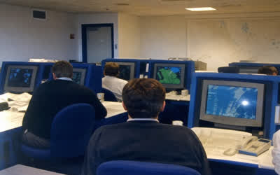 A low-resolution operations room with CRT monitors and anonymous operators.